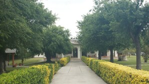 A pathway flanked by neatly trimmed hedges and trees, leading to a building with a tiled roof. - Relais La Mimosa (Sabaudia)
