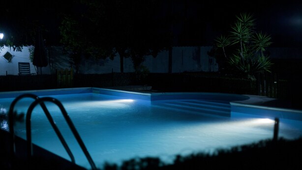 A nighttime swimming pool with a dark surrounding area and a few trees. - Relais La Mimosa (Sabaudia)