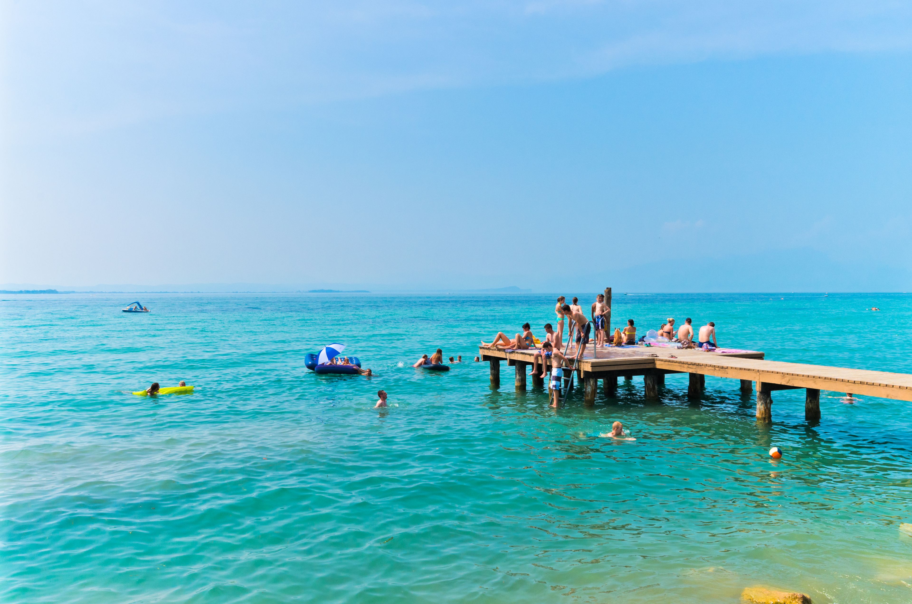 Un muelle que se adentra en un mar azul y transparente, con gente nadando y tomando el sol.