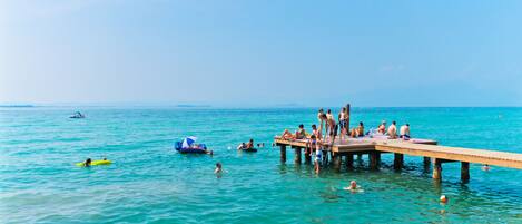 Un muelle que se adentra en un mar azul y transparente, con gente nadando y tomando el sol.