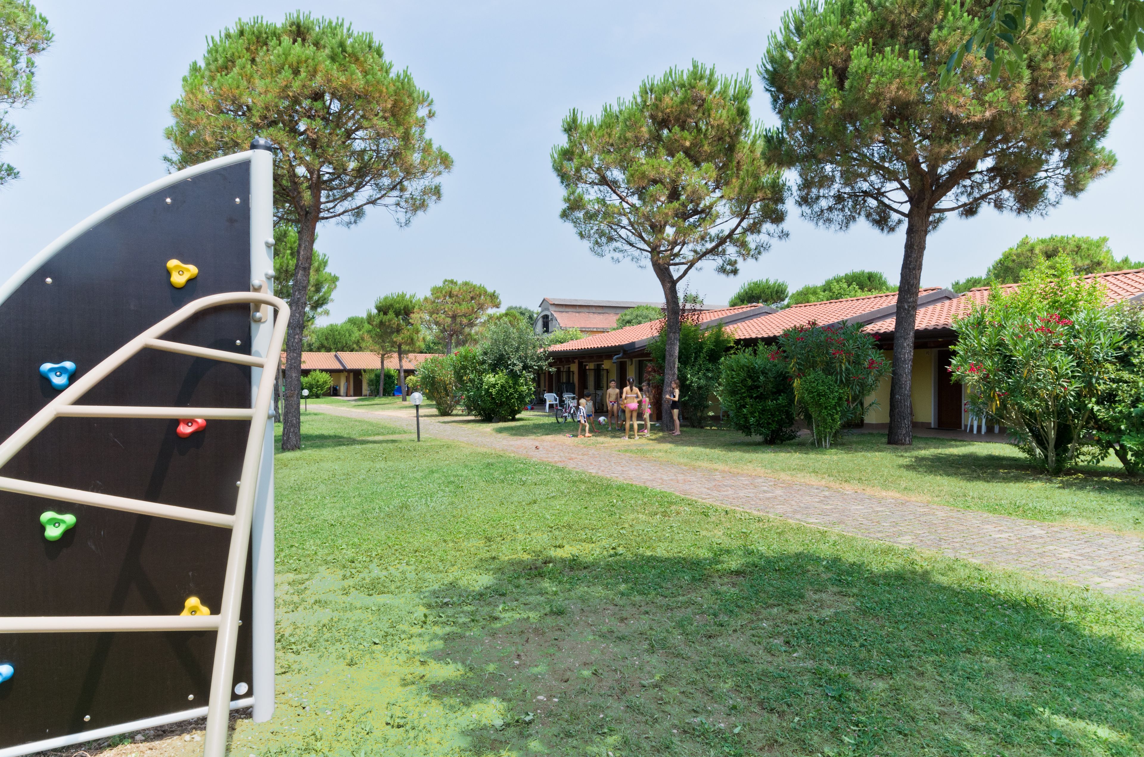 A playground with climbing structures and a paved pathway leading to a building with a red-tiled roof.