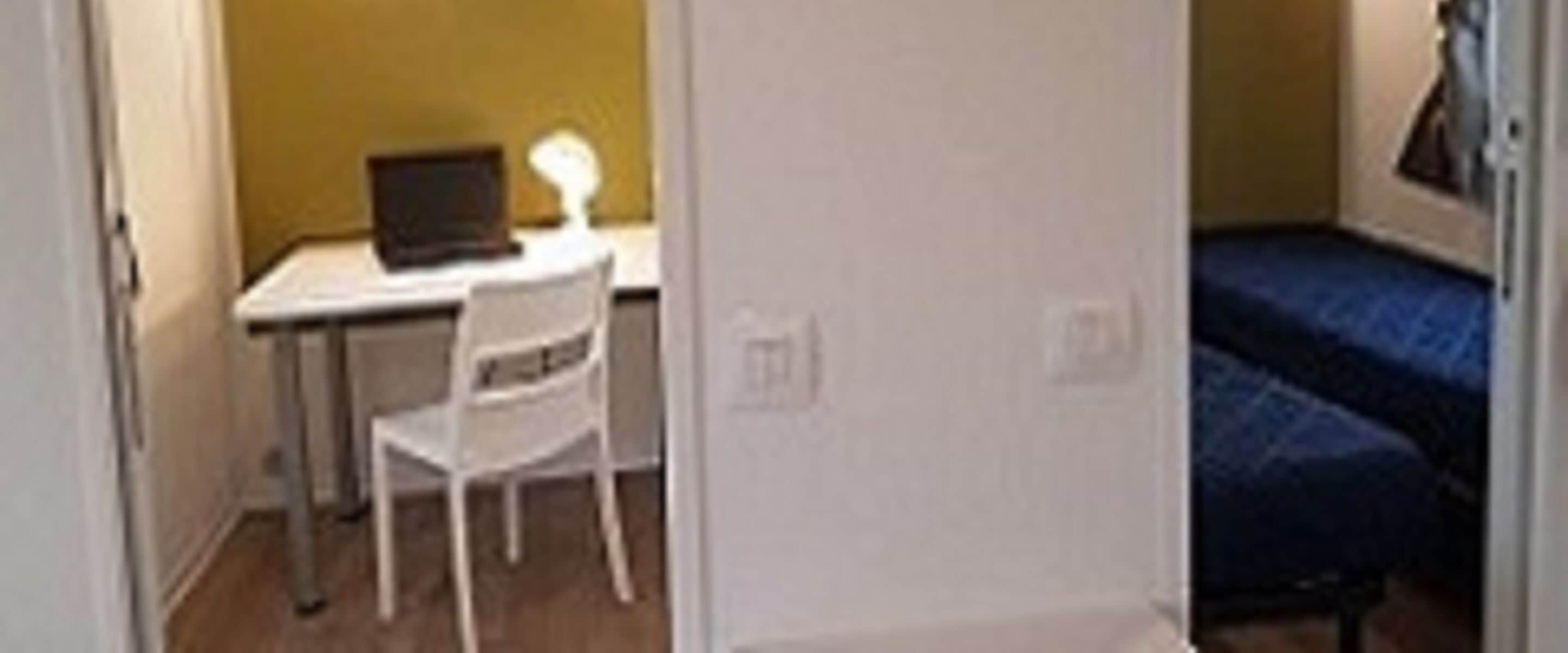 A small room with a desk, chair, and a bed.