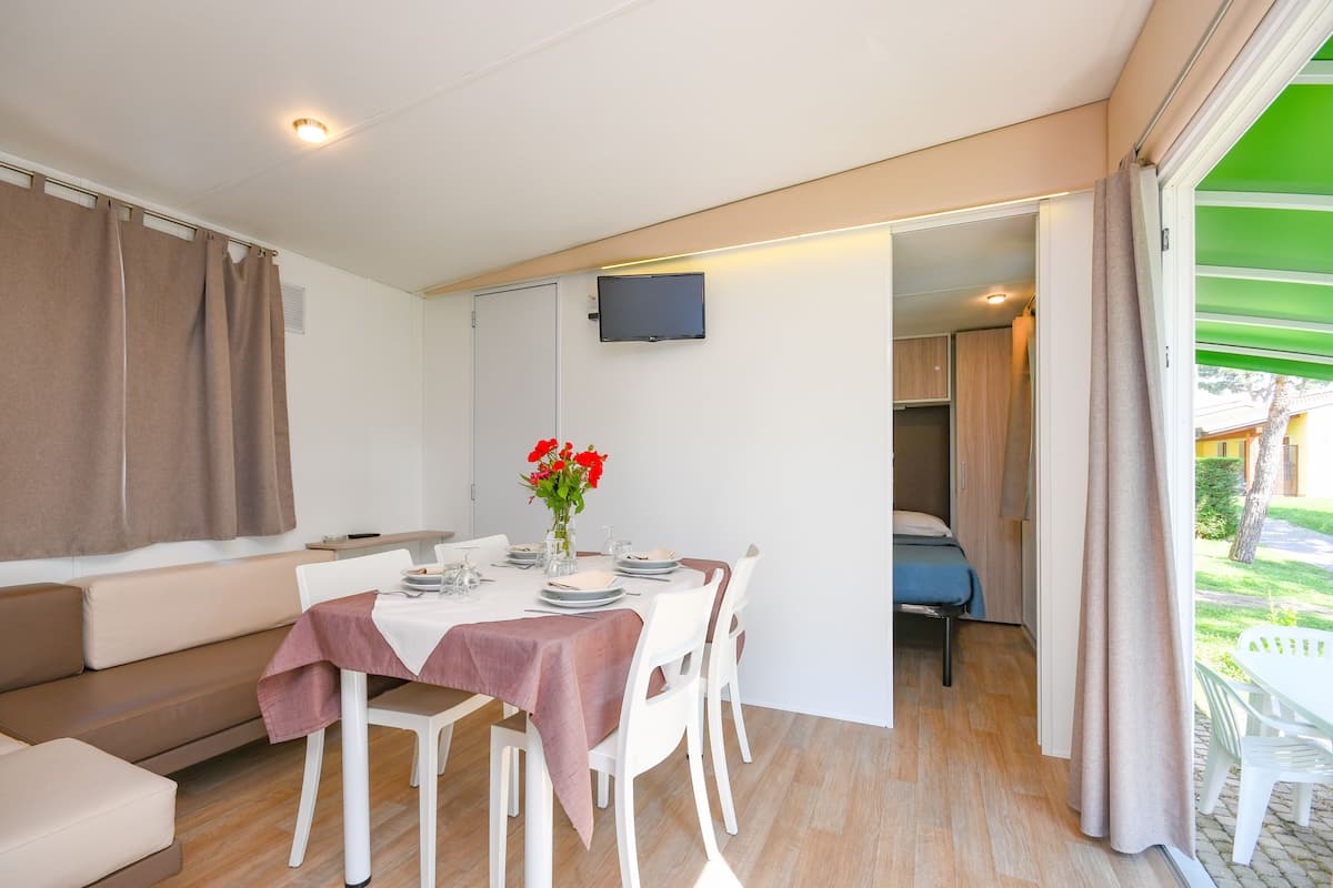 Un área de comedor con una mesa preparada para cuatro personas, un sofá y un televisor montado en la pared.