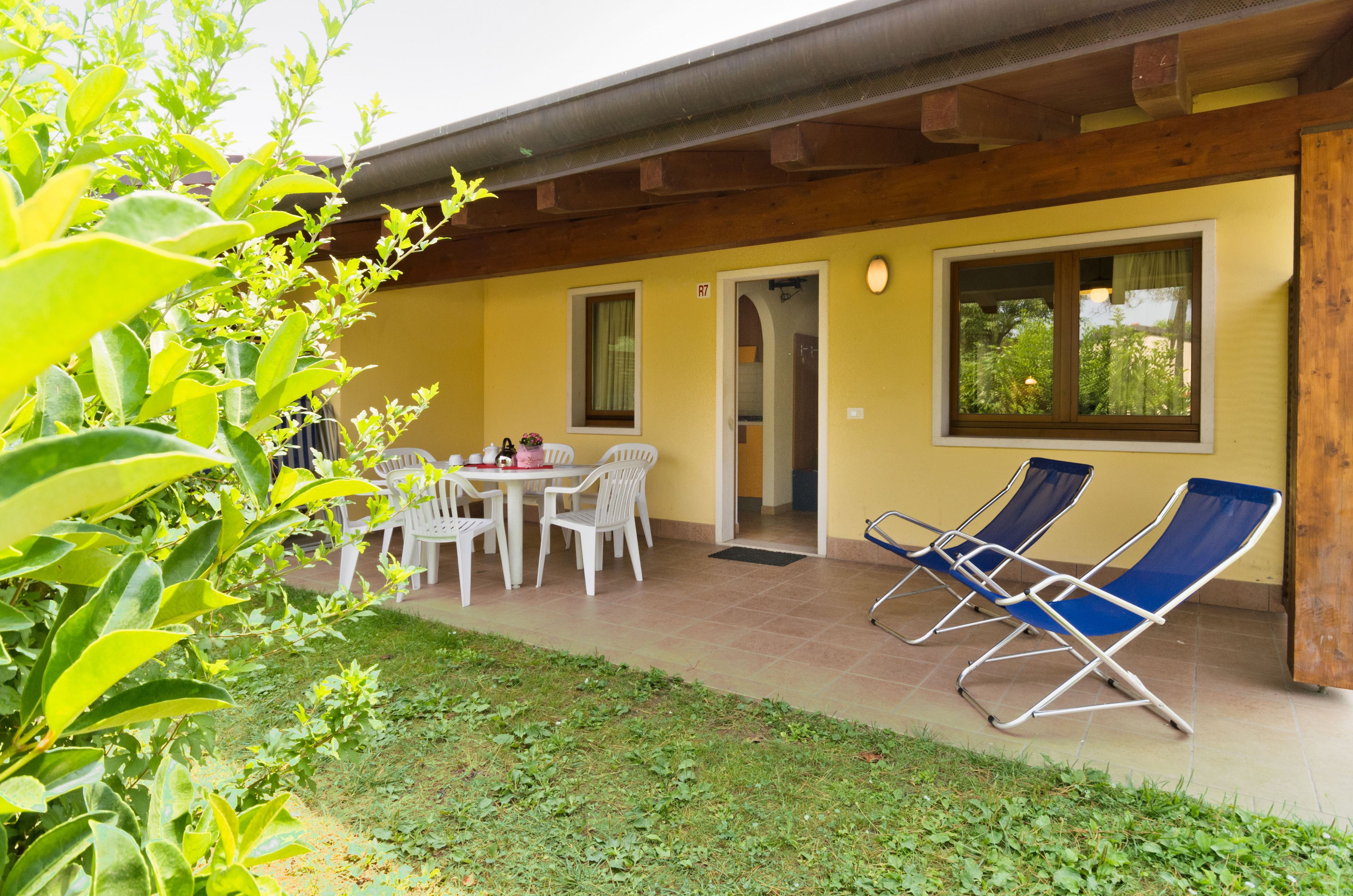 Un patio techado con una mesa y sillas, una puerta que da a una habitación y dos sillones.