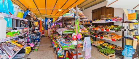Un mercado interior muy iluminado, con varios puestos que venden productos como frutas, verduras y artículos para el hogar.