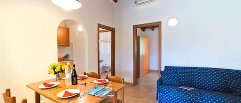 A dining area with a wooden table set for four, a blue sofa, and a kitchen visible through an archway.