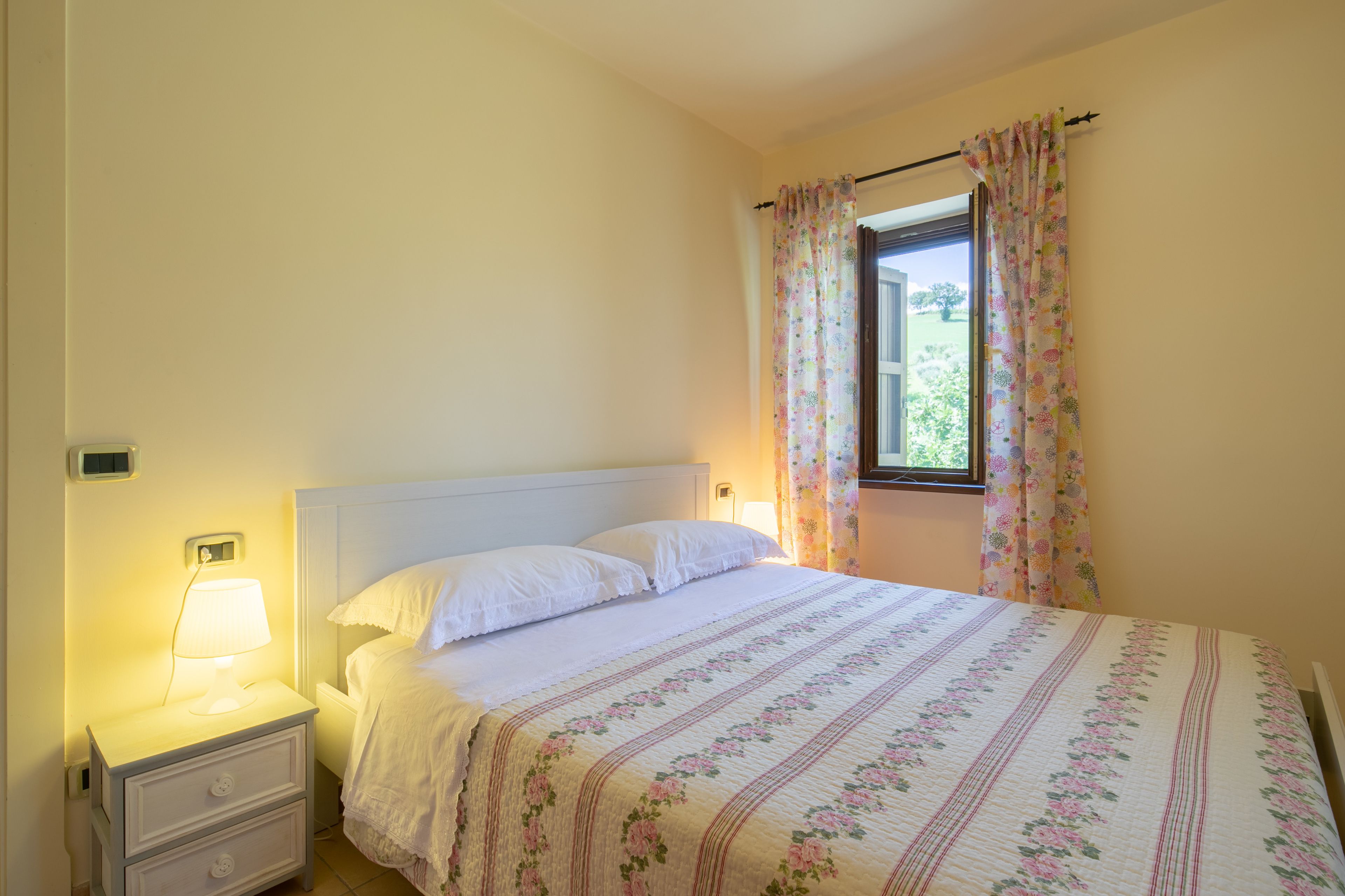 A bedroom with a bed, a nightstand, a lamp, and a window with curtains.