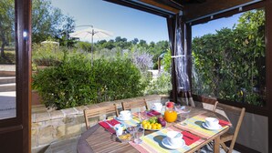 Un espace de restauration en plein air avec une table dressée pour le petit-déjeuner, entouré de murs en pierre et de verdure.