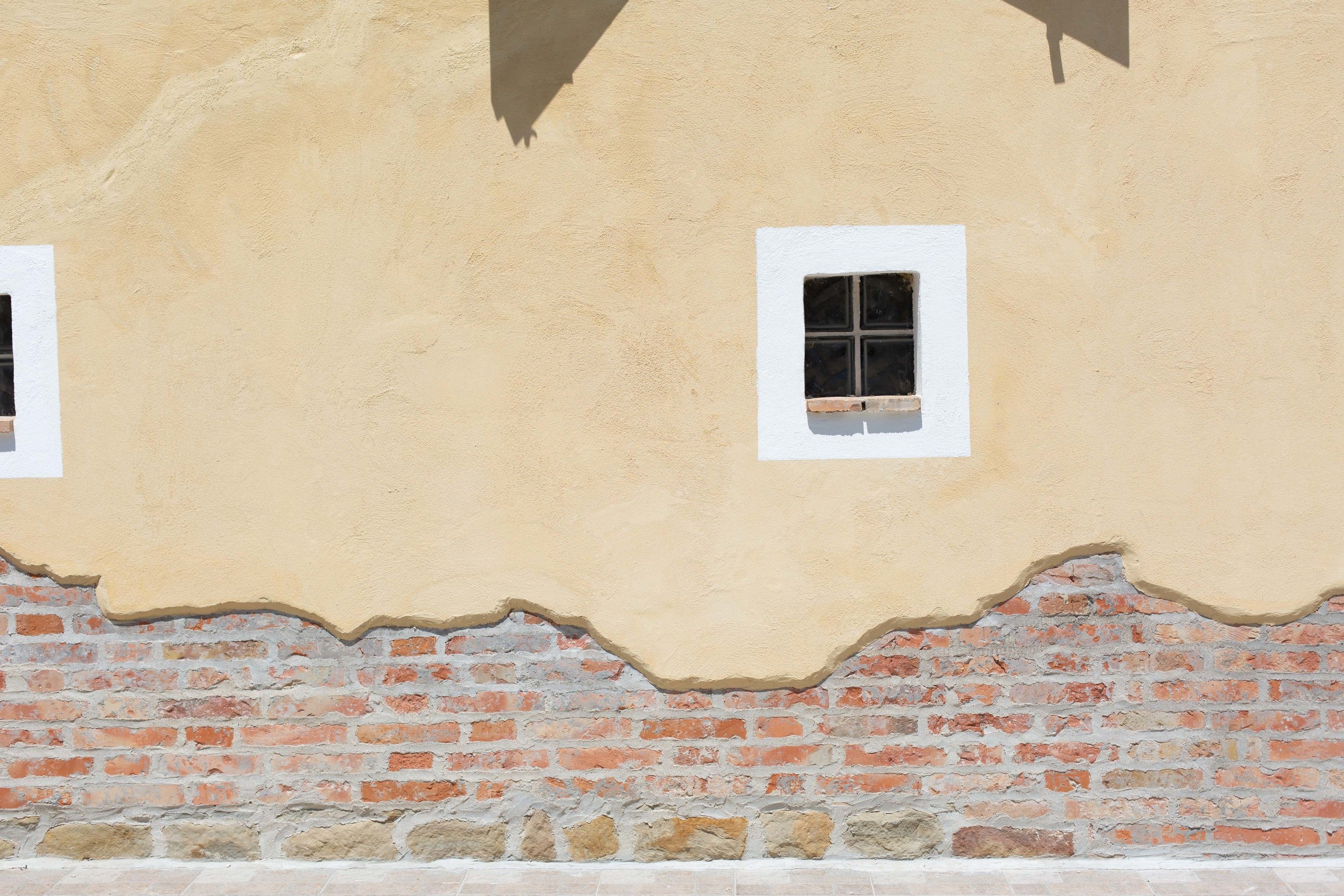A building facade with a textured beige wall and a lower section of exposed red brickwork.