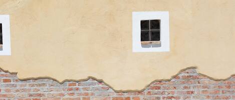 A building facade with a textured beige wall and a lower section of exposed red brickwork.