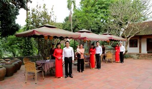 A group of people standing under a covered patio area with a brick floor and potted plants. - Moon Garden Homestay (Hanoi)