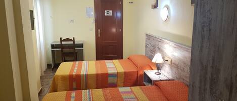Una habitación de hotel con dos camas, un escritorio, una silla, una lámpara y una puerta.