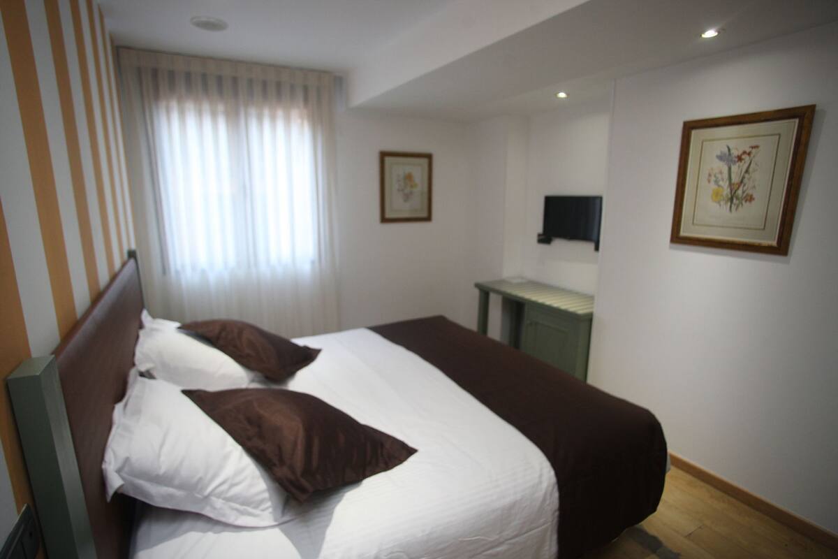 A hotel room with a bed, a desk, a television, and a window with curtains.