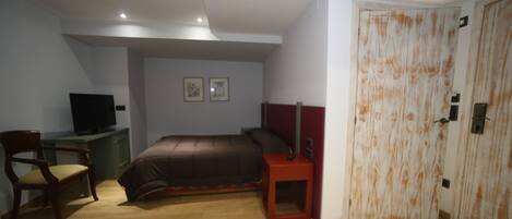 Un dormitorio con cama, escritorio con silla, televisor y armario.