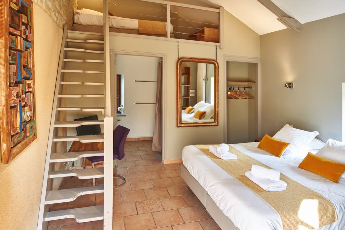 Une chambre avec un lit superposé, un escalier, un miroir et une armoire.