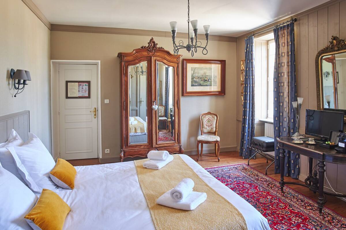 Une chambre d’hôtel avec un grand lit, une armoire en bois, un bureau avec un ordinateur et un grand miroir.