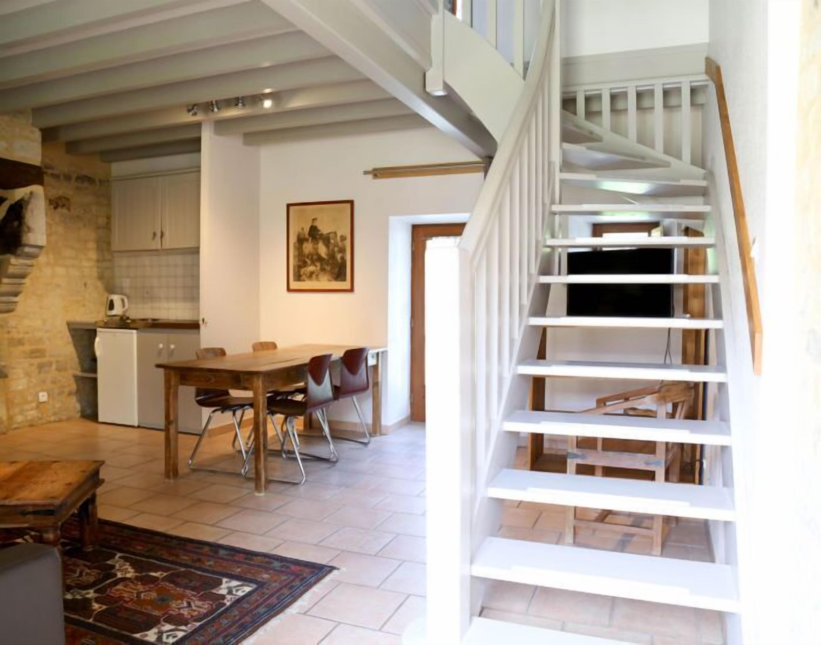 Un vaste espace de vie comprenant une table à manger, des chaises, un escalier et, au fond, une cuisine.