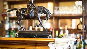 Angolo bar con una statua in bronzo di un uomo a cavallo, un bancone in legno e scaffali pieni di bottiglie sullo sfondo.
