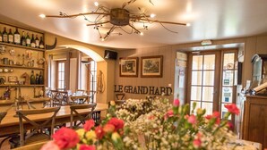 Un interior de restaurante con zona de bar, muebles de madera y un letrero que dice "LE GRAND HARD".