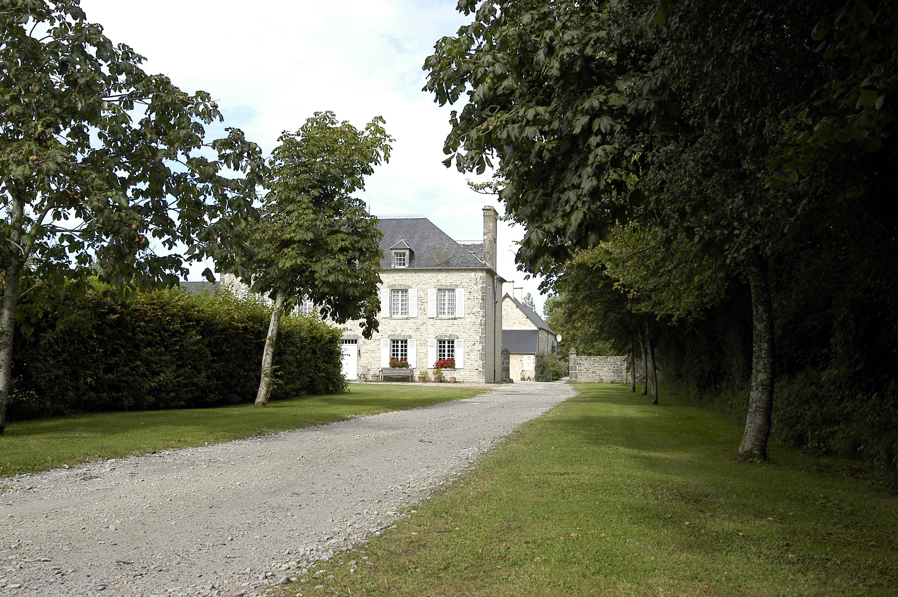 A stone building with a gravel driveway, surrounded by trees and grass.
