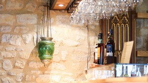 Zona de bar con pared de piedra, taburetes de madera y una lámpara colgante.
