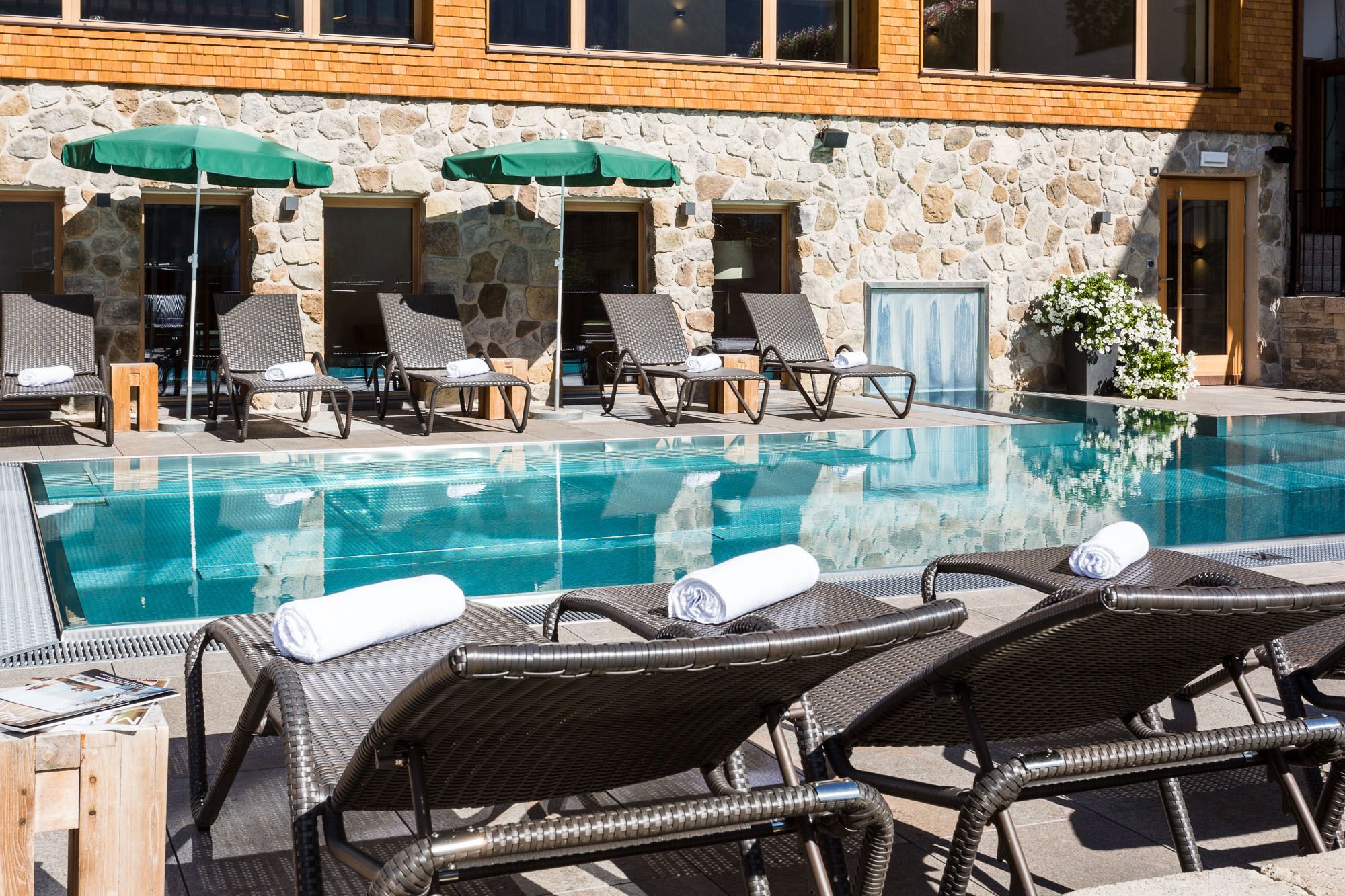 A poolside area with lounge chairs and umbrellas, a stone building with a wooden door, and a clear blue pool.