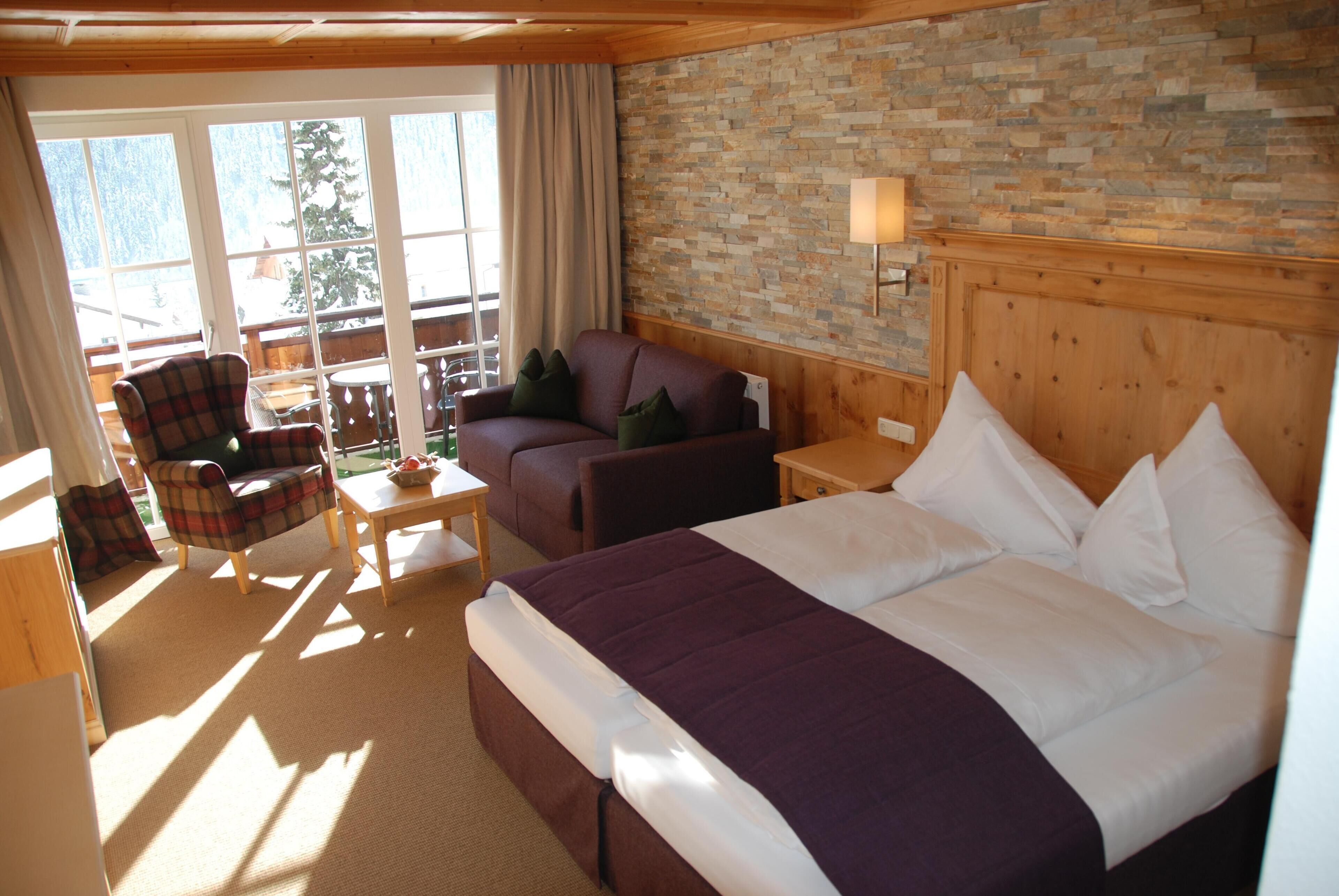 Habitación de hotel con una cama grande, un sofá, una silla, una mesita y una pared de piedra.