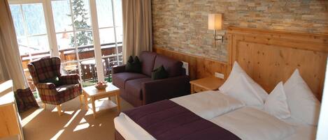 Habitación de hotel con una cama grande, un sofá, una silla, una mesita y una pared de piedra.