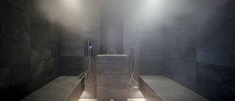 A modern, dimly lit shower area with dark stone walls and a central rectangular platform.