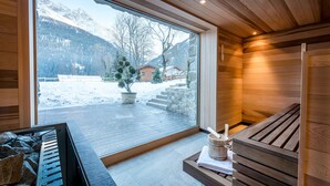 Un sauna con un banco de madera, un lavamanos de piedra y vistas a un paisaje montañoso nevado.