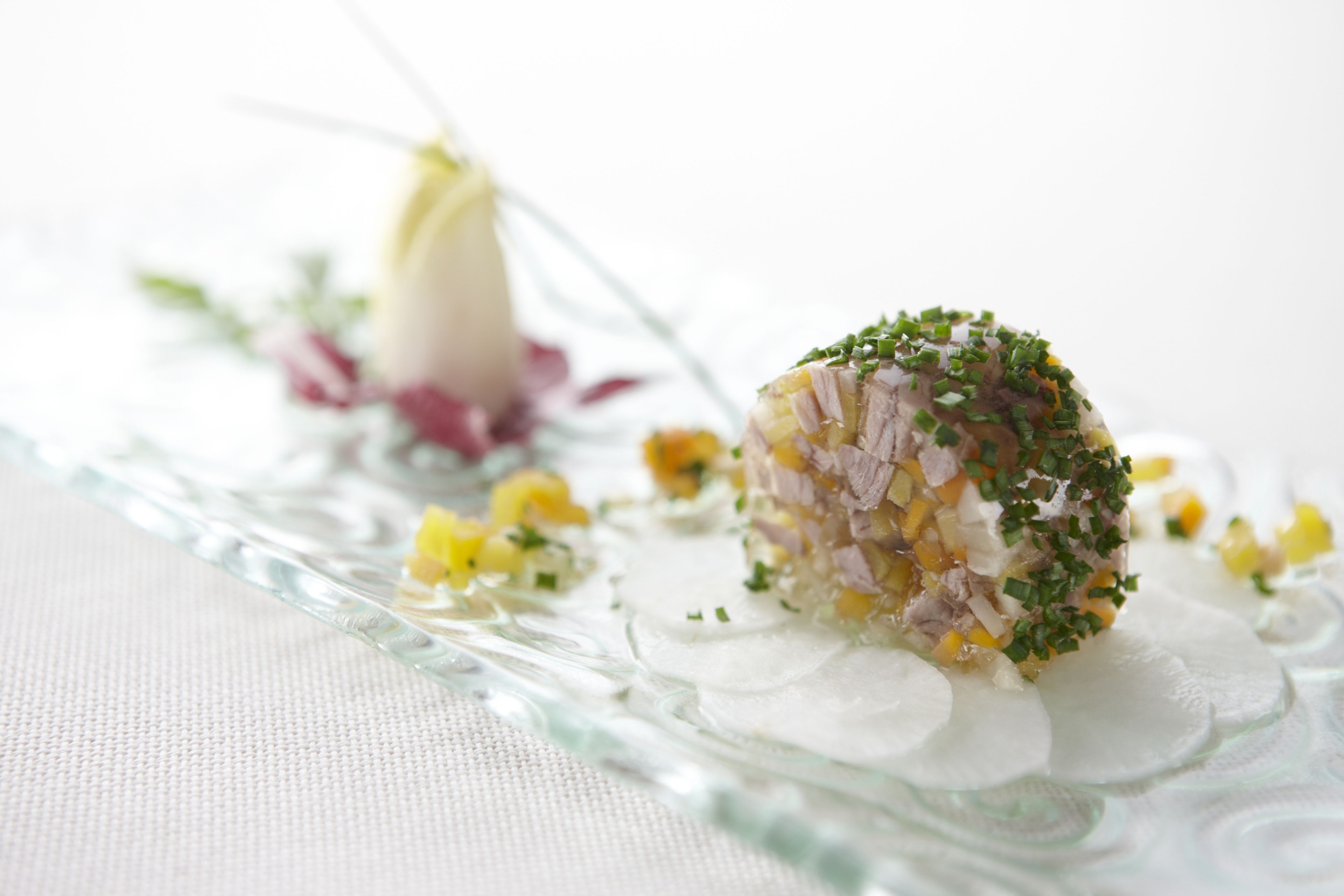 A glass dish with a food item garnished with herbs, accompanied by a flower and small yellow elements.
