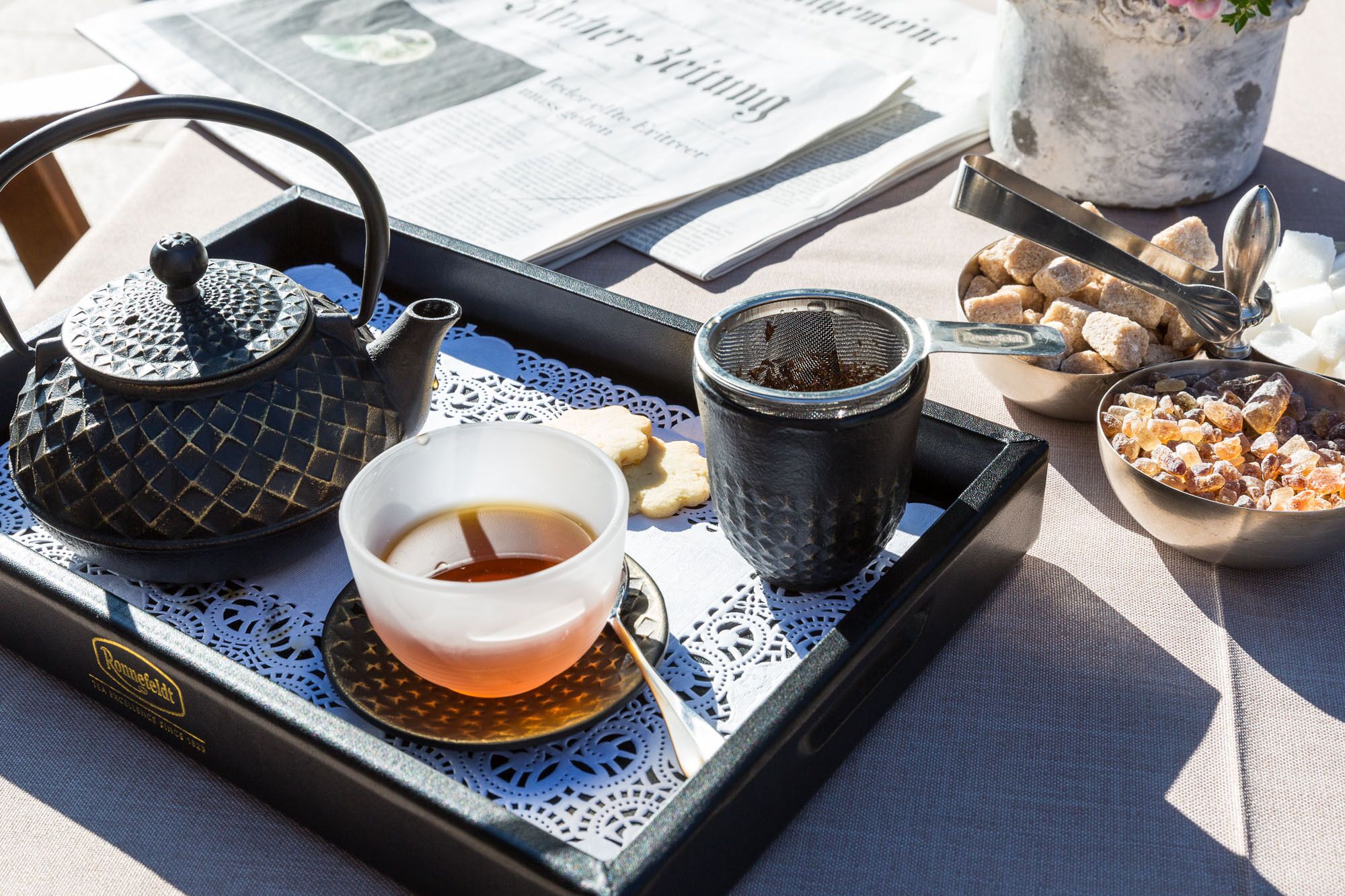 Un plateau avec une théière, une tasse de thé, un sucrier et un sachet de sucre.