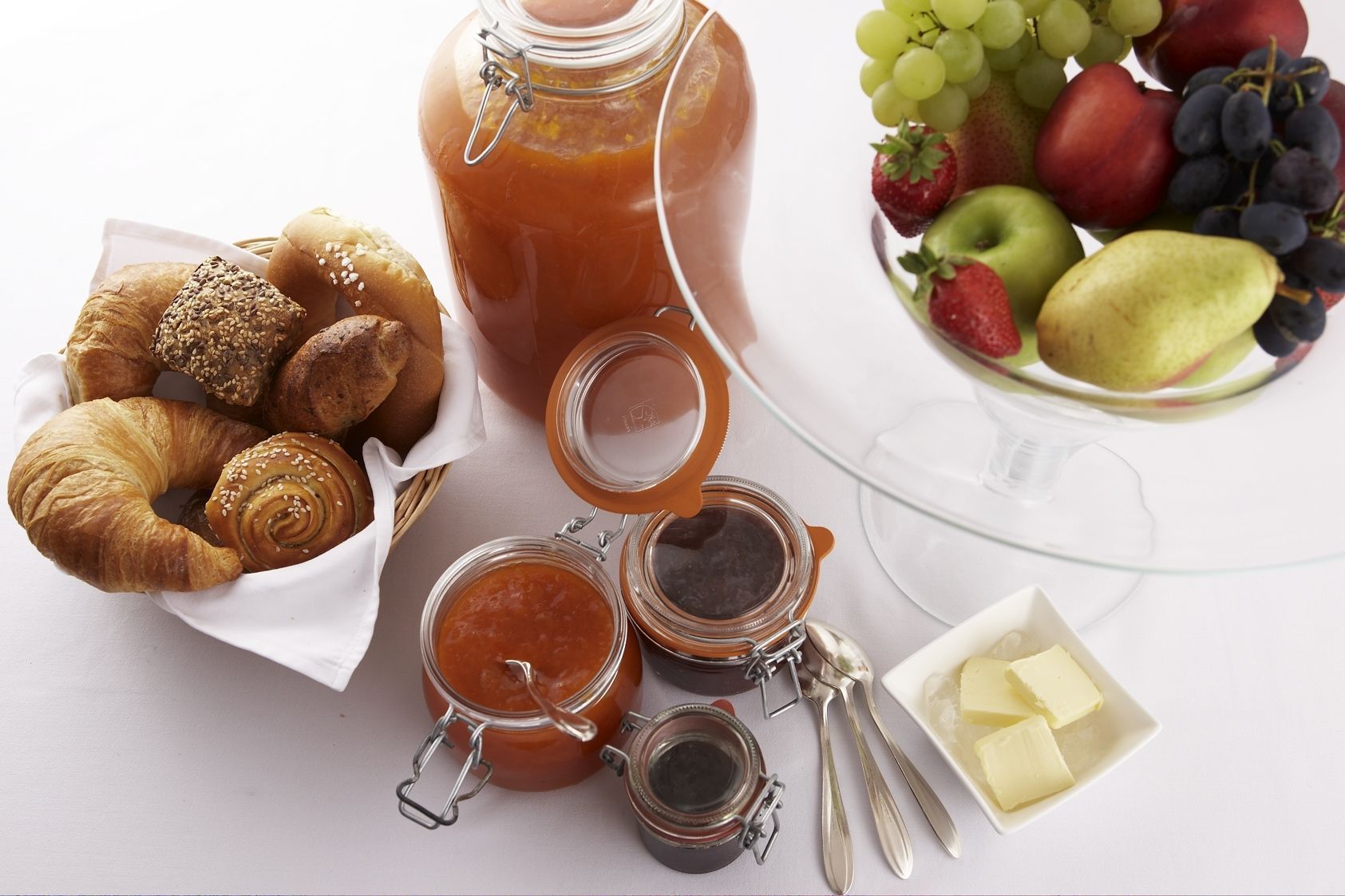Een ontbijtsetting met croissants, jam, boter en een fruitschaal.