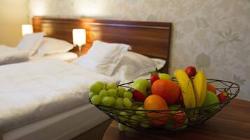 Habitación de hotel con dos camas, una mesita de noche con un frutero que contiene uvas, fresas, naranjas y plátanos.