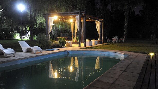 A swimming pool with lounge chairs and a covered seating area at night. - Pilgrim's Rest (Chacras de Coria)