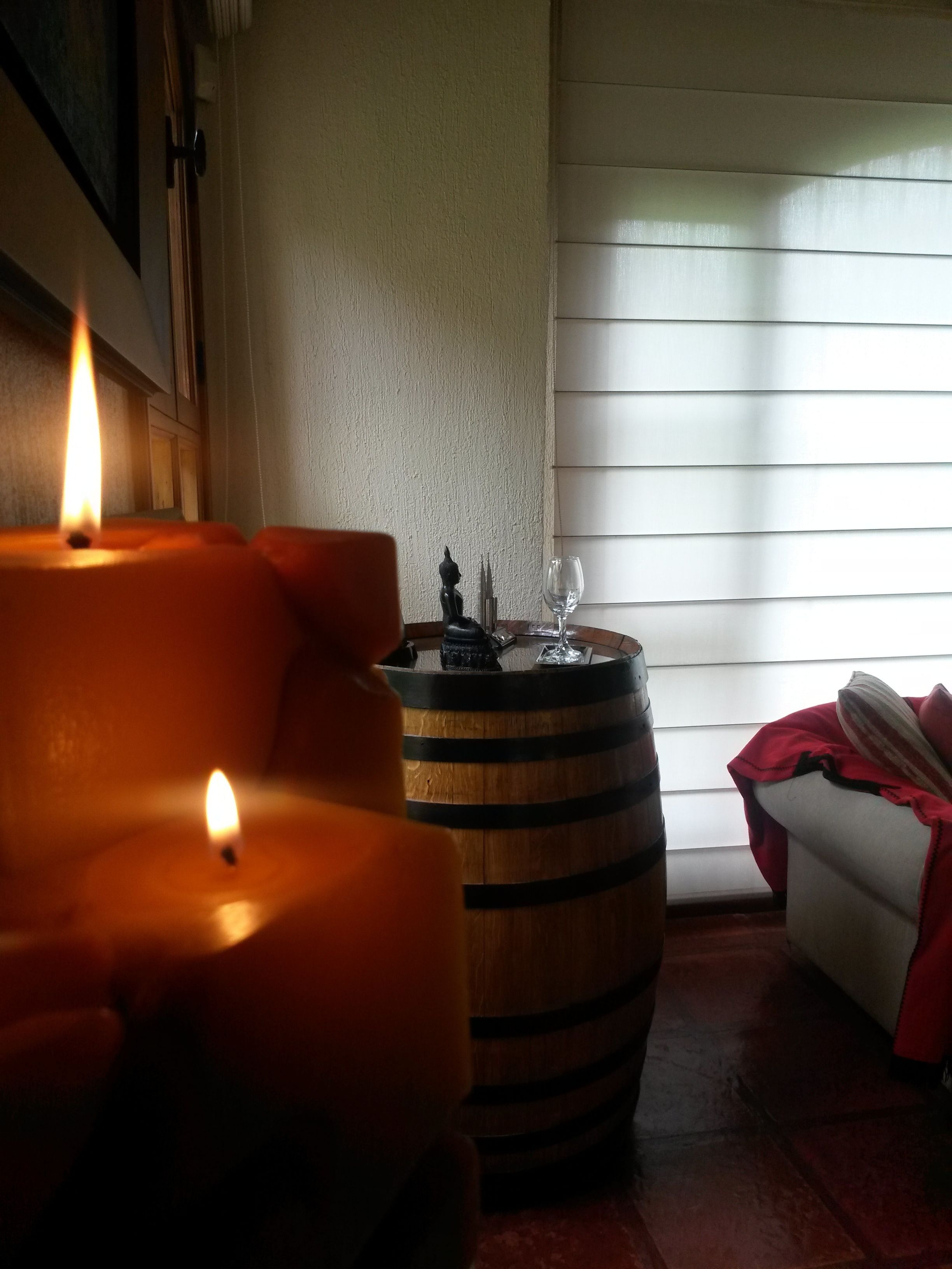 A room with a lit candle, a wooden barrel, and a white couch with a red blanket.