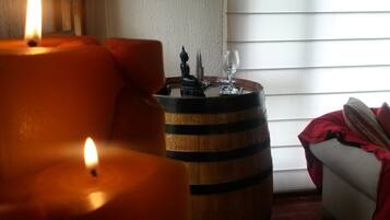 A room with a lit candle, a wooden barrel, and a white couch with a red blanket.