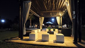 An outdoor seating area with cushioned benches and tables, under a covered structure with draped curtains. - Pilgrim's Rest (Chacras de Coria)