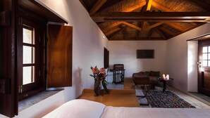 Una habitación con una cama, techo de madera, una mesita con velas y un florero con flores.