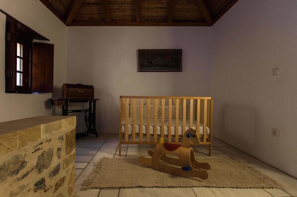 Une pièce avec un berceau en bois, un cheval à bascule, un mur en pierre et un tableau encadré accroché au mur.