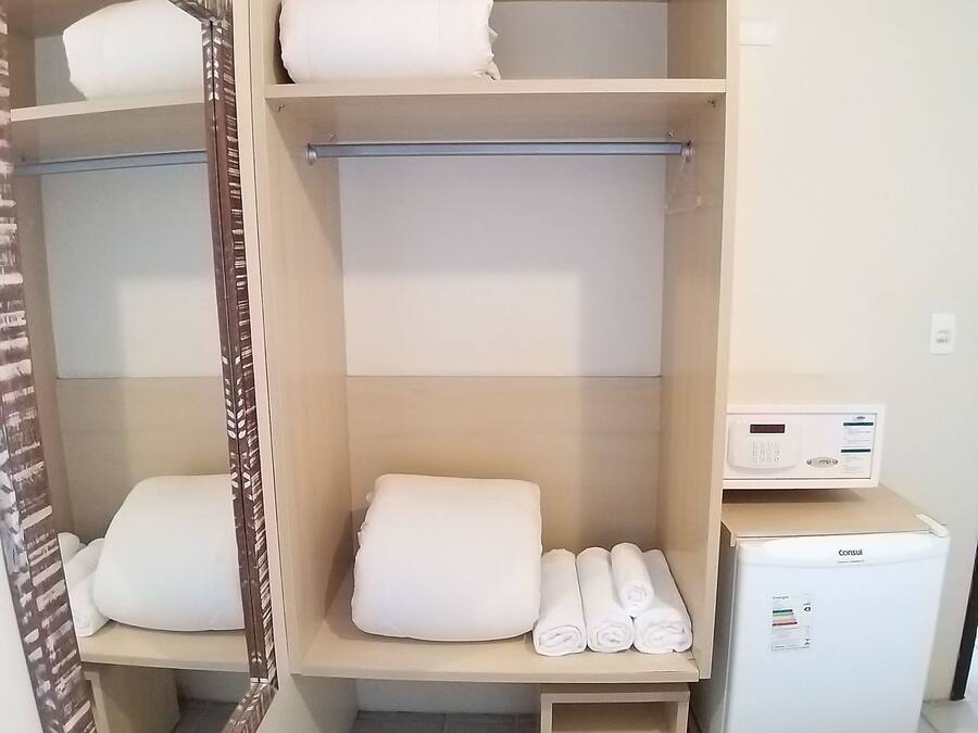 Une chambre d’hôtel équipée d’un placard contenant des serviettes pliées, d’un miroir et d’un petit réfrigérateur.