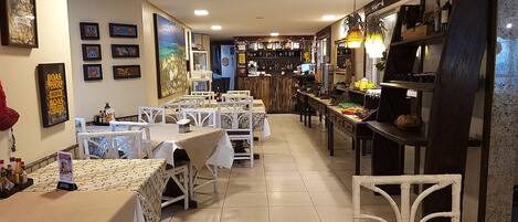 A restaurant with multiple tables and chairs, a bar area, and various framed pictures on the walls.