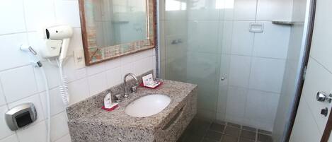 Un baño con lavamanos de granito, un espejo, un secador de pelo de mano y una cabina de ducha.