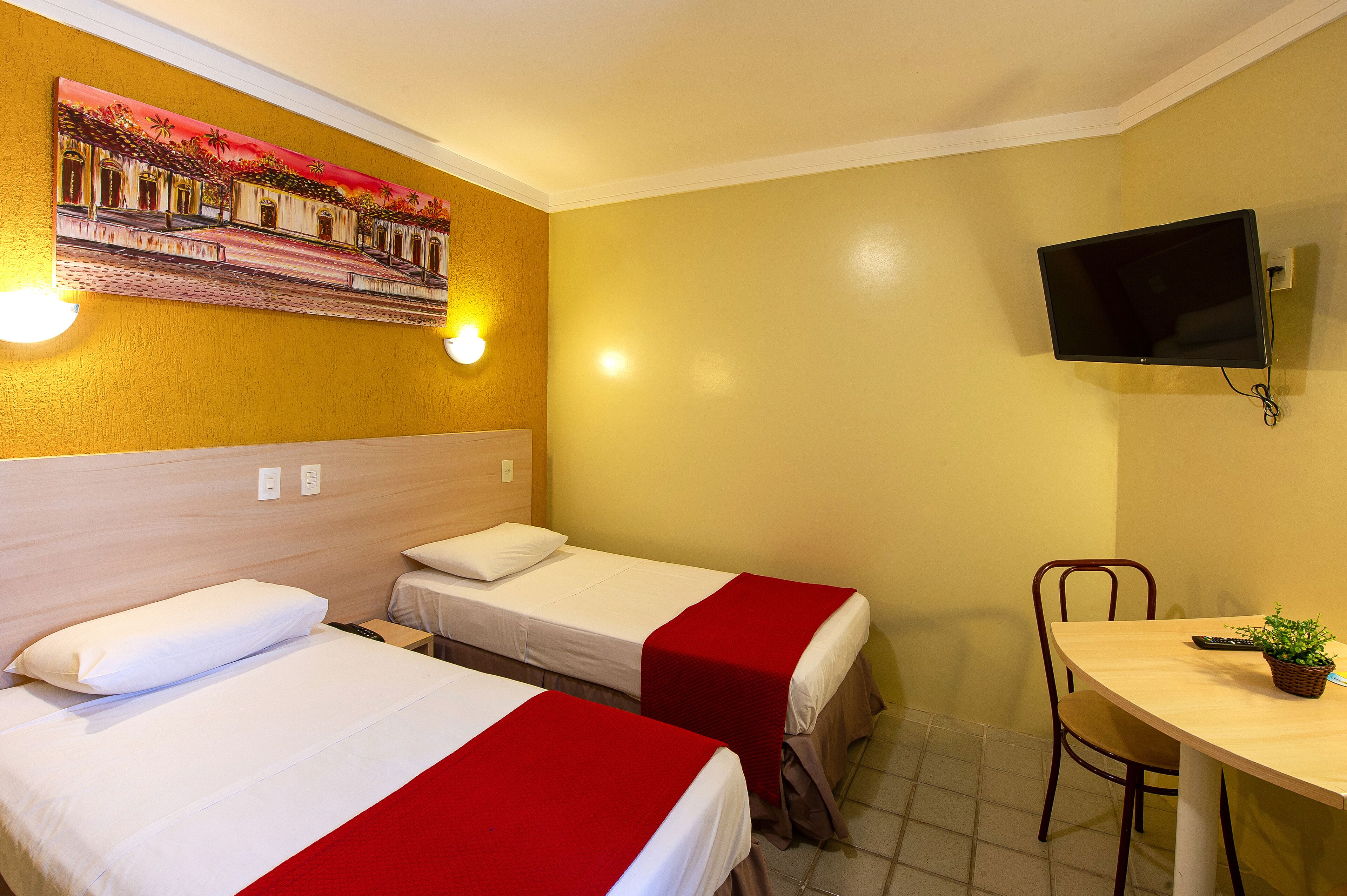 Habitación de hotel con dos camas, un televisor, un escritorio con una silla y un televisor montado en la pared.