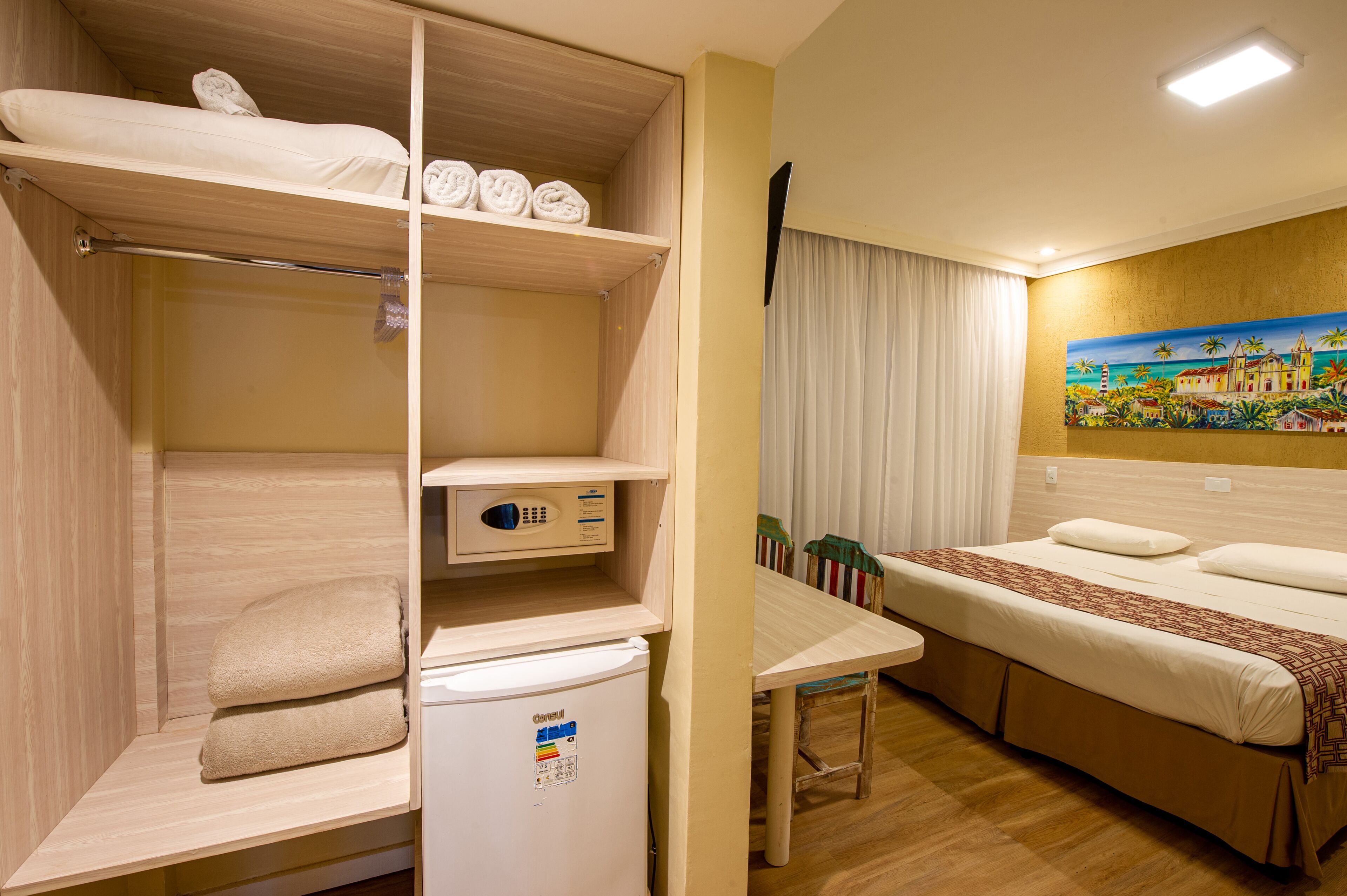Una habitación de hotel con literas, una mesita pequeña, un refrigerador y un cuadro en la pared.