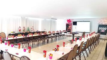 Uma sala de conferências com mesas compridas, cadeiras e uma tela de projeção.