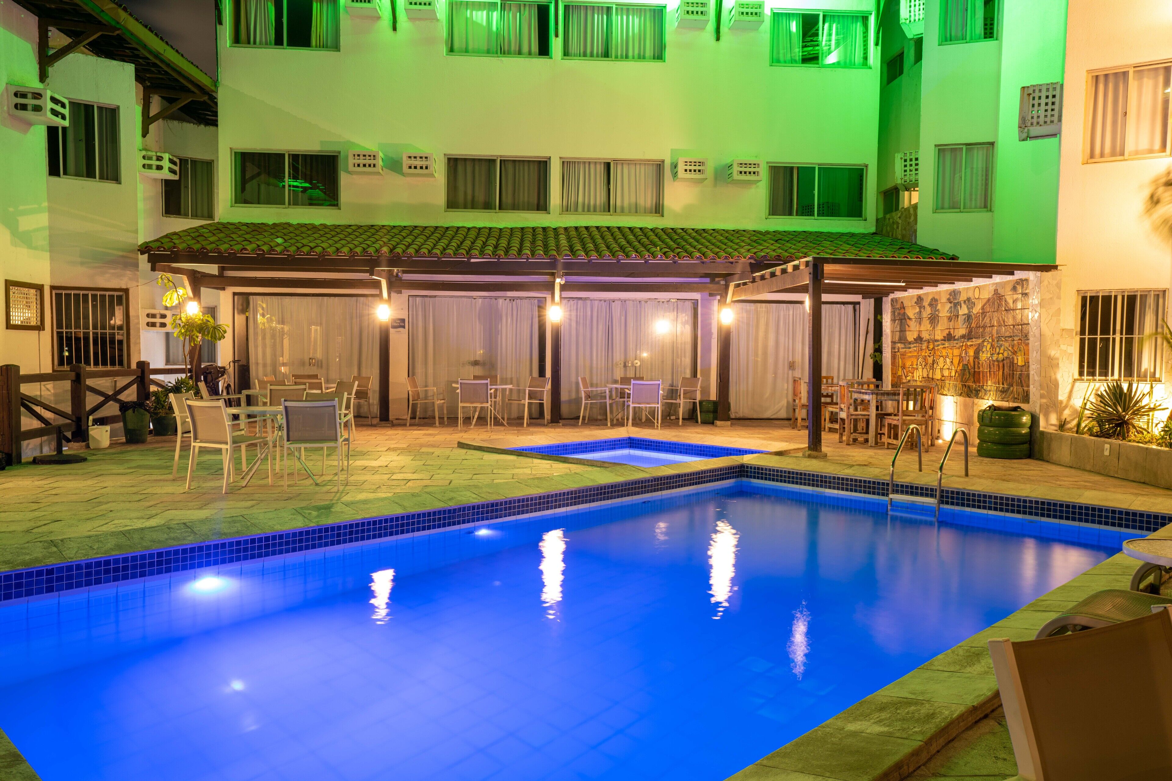 A swimming pool with a tiled edge, surrounded by outdoor seating and a covered patio area.