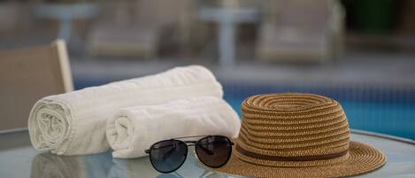 Una mesa de vidrio con una toalla blanca enrollada, un sombrero de paja y gafas de sol.