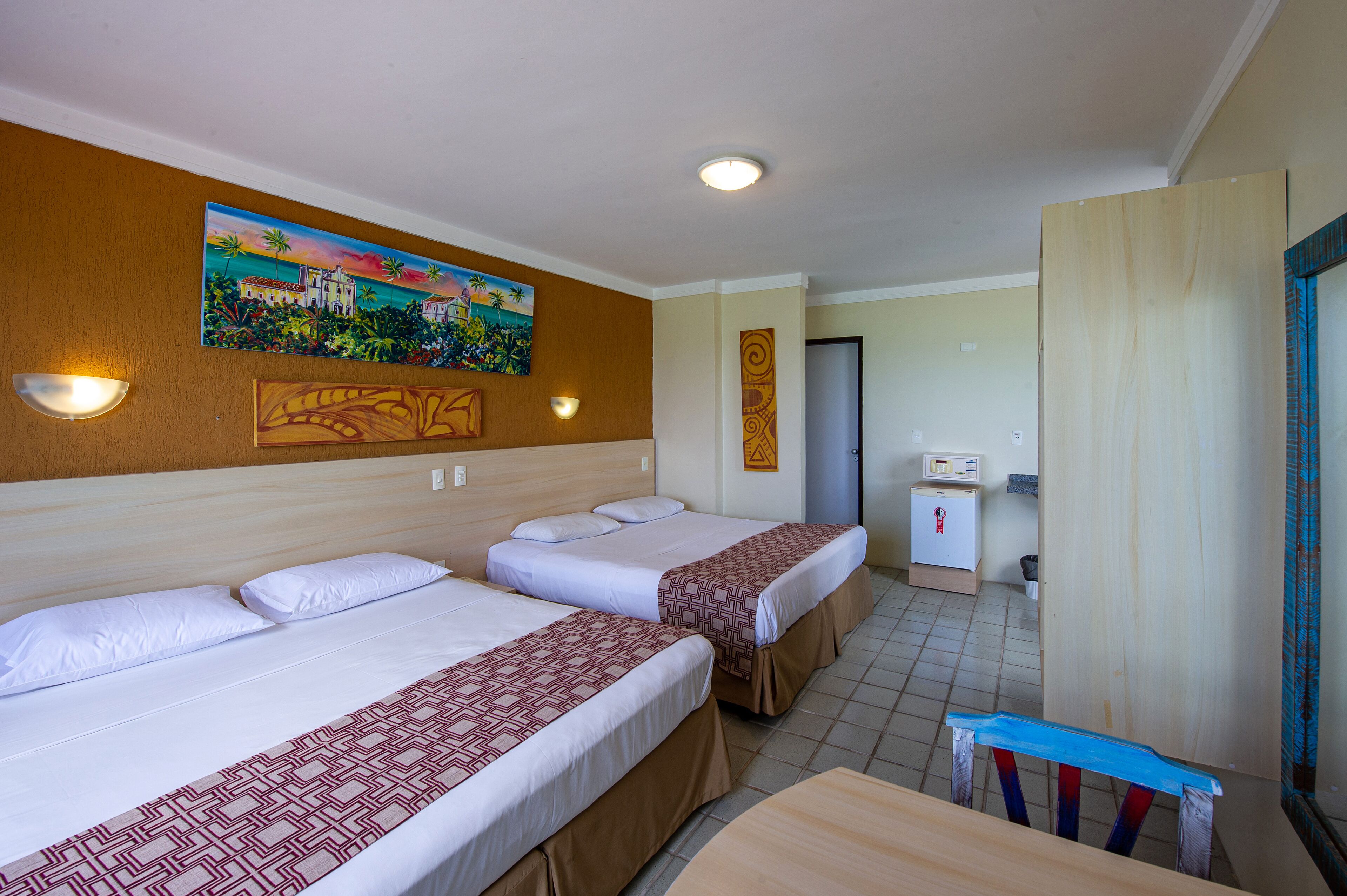 A hotel room with two beds, a painting on the wall, a minibar, and a desk with a chair.