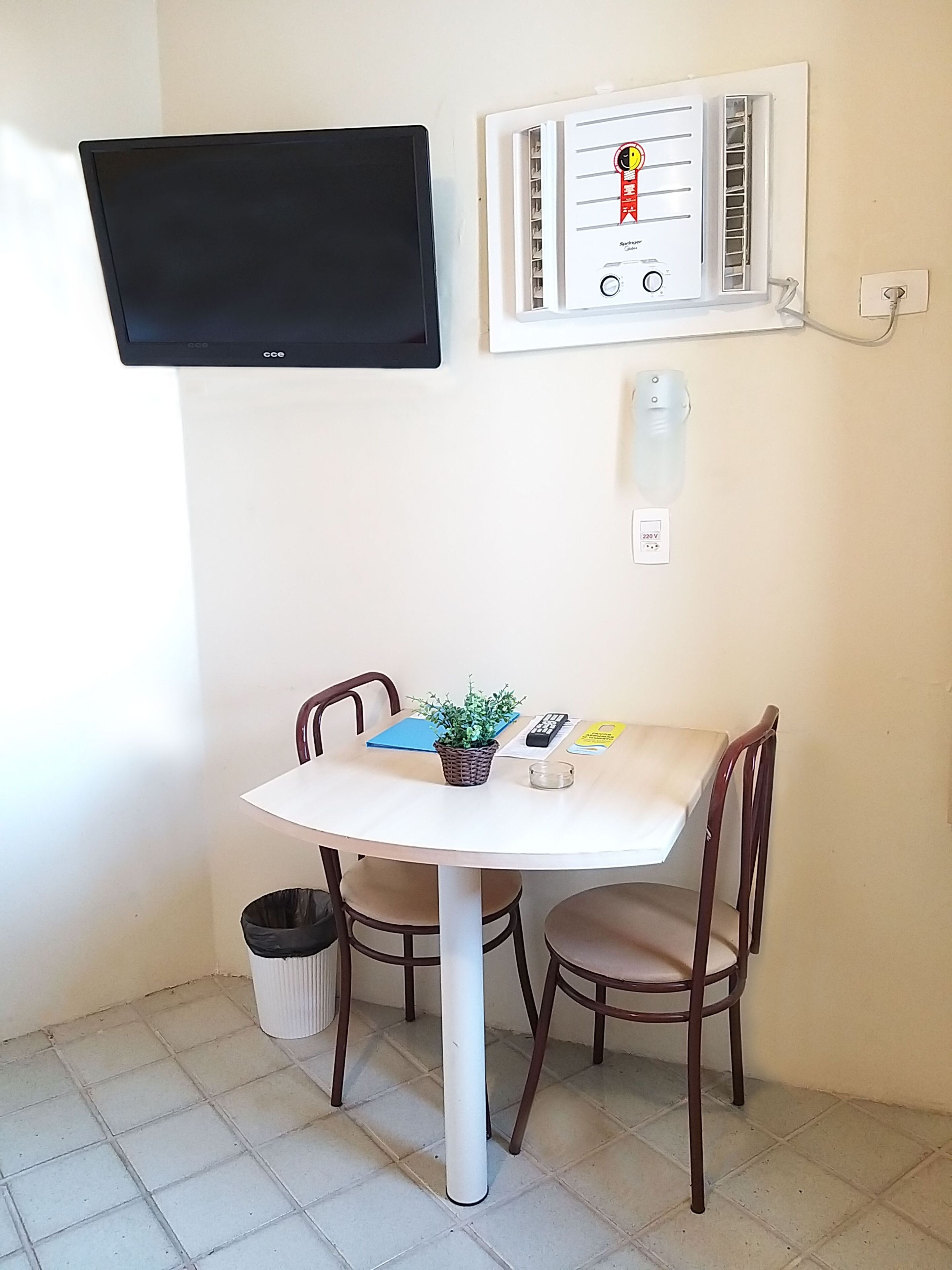 A small dining area with a table, chairs, a television mounted on the wall, and an air conditioning unit.